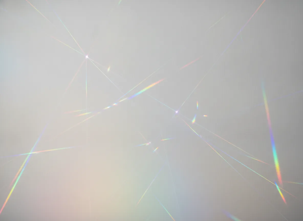 Clean neutral backdrop overlaid with refracted rainbow prism light streaks and soft chromatic flares spilling across the surface. Modern, luminous, and artistic.